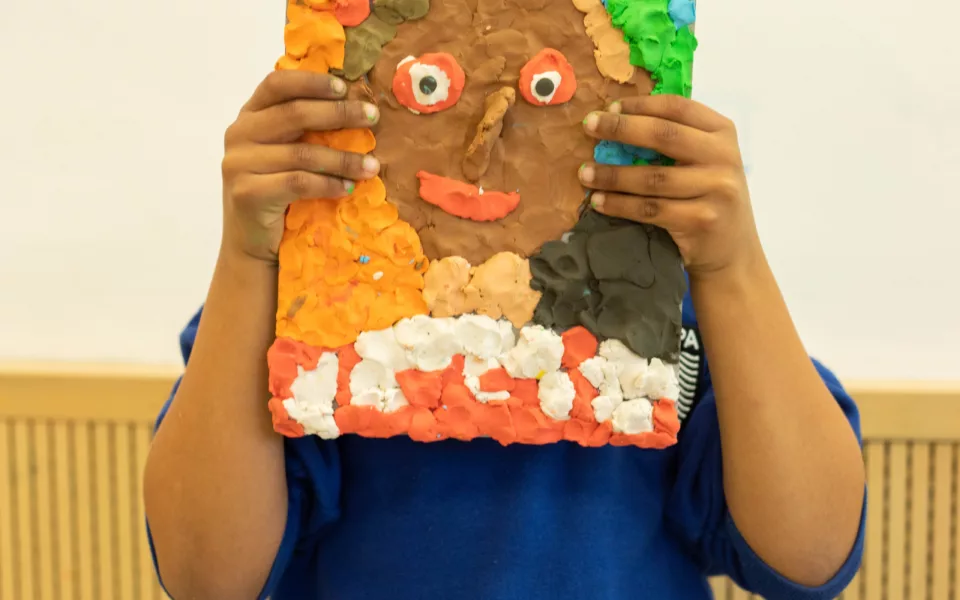 A child holds up a Plasticine painting of a face