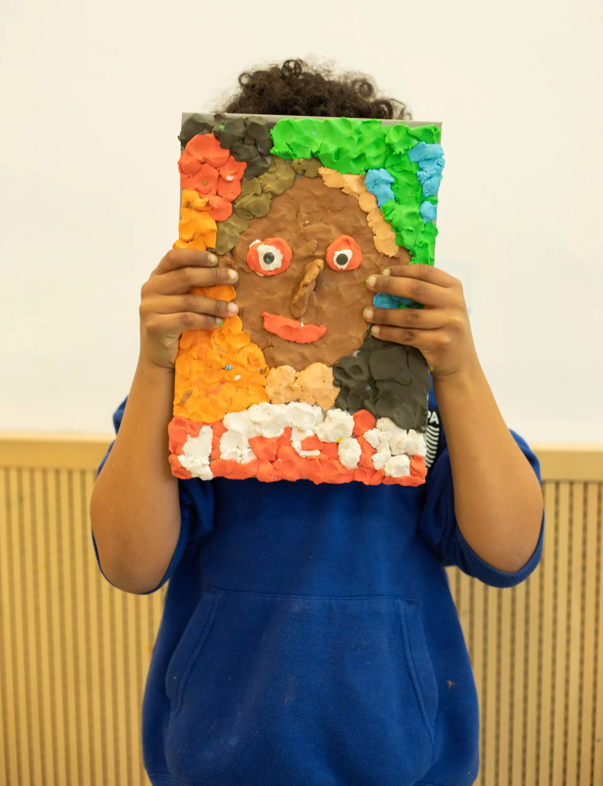 A child holds up a Plasticine painting of a face