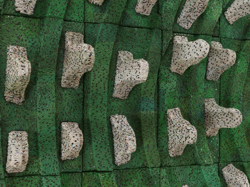 A colour photograph of Elias Sime's three-dimensional piece made from woven electrical wire in a bright earthy green, shades of beige and coral pink.